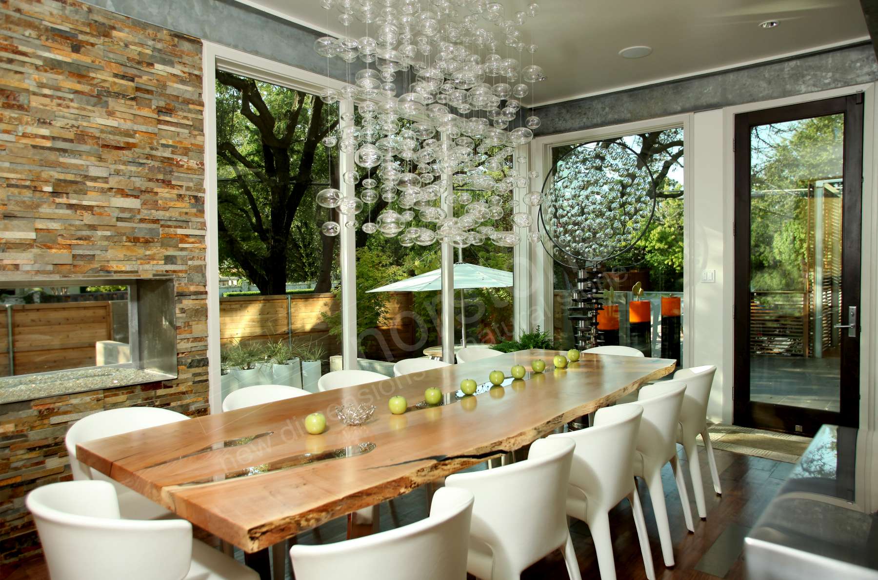 Norstone Ochre Rock Panels on a see through fireplace on a wall in a beautiful dining room with a large wood table and multiple floor to ceiling glass windows and a bubble style light fixture